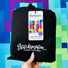 Load image into Gallery viewer, Black cross stitch kit pouch held by a hand with a colorful geometric pattern in the background