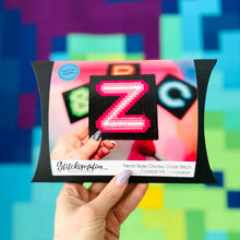 Load image into Gallery viewer, Hand holding a cross-stitch kit with 'Z' design against a colorful geometric background
